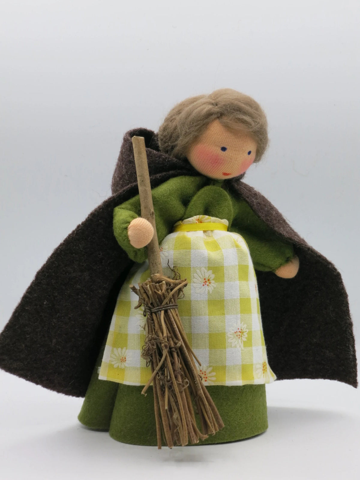 Frontalansicht von Fräulein Tau aus Wollfilz mit grünem Kleid, offenem braunen Umhang, Besen und Blütenschürzchen.