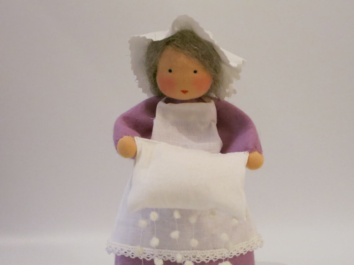 Detailansicht der Märchenfigur Frau Holle aus Wollfilz mit weißem Kissen, lila Ärmel und Schürze mit Schneeflocken.