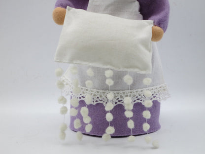 Detail der Frau-Holle-Figur aus Wollfilz mit weißem Kissen, bestickter Schneeflockenschürze und lila Kleid.