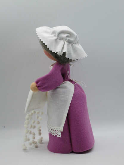 Seitenansicht der Frau-Holle-Figur aus Wollfilz mit lila Kleid, weißer Haube, Schürze und Schneeflockenkette.