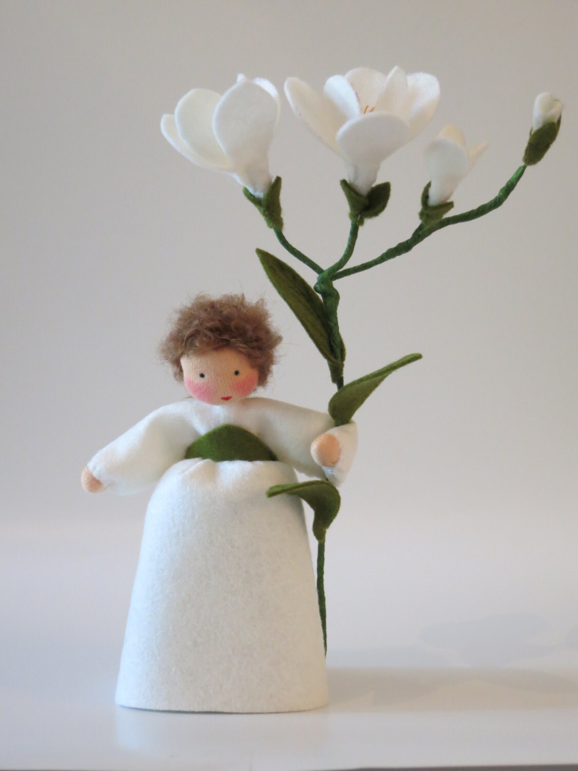 Handgefertigtes Freesien-Blumenkind aus Wollfilz mit weißem Kleid, grünen Blättern und Zweig mit weißen Freesienblüten.