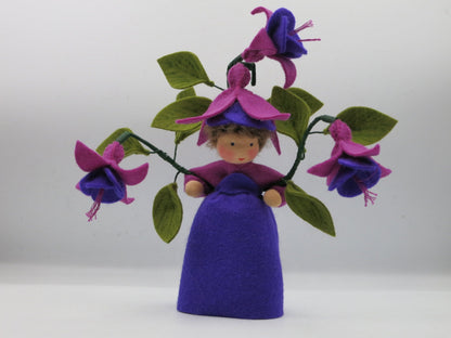 Handgefertigtes Fuchsien-Blumenkind aus Wollfilz mit violettem Kleid, Fuchsienblüten, grünen Blättern und Blütenhut.