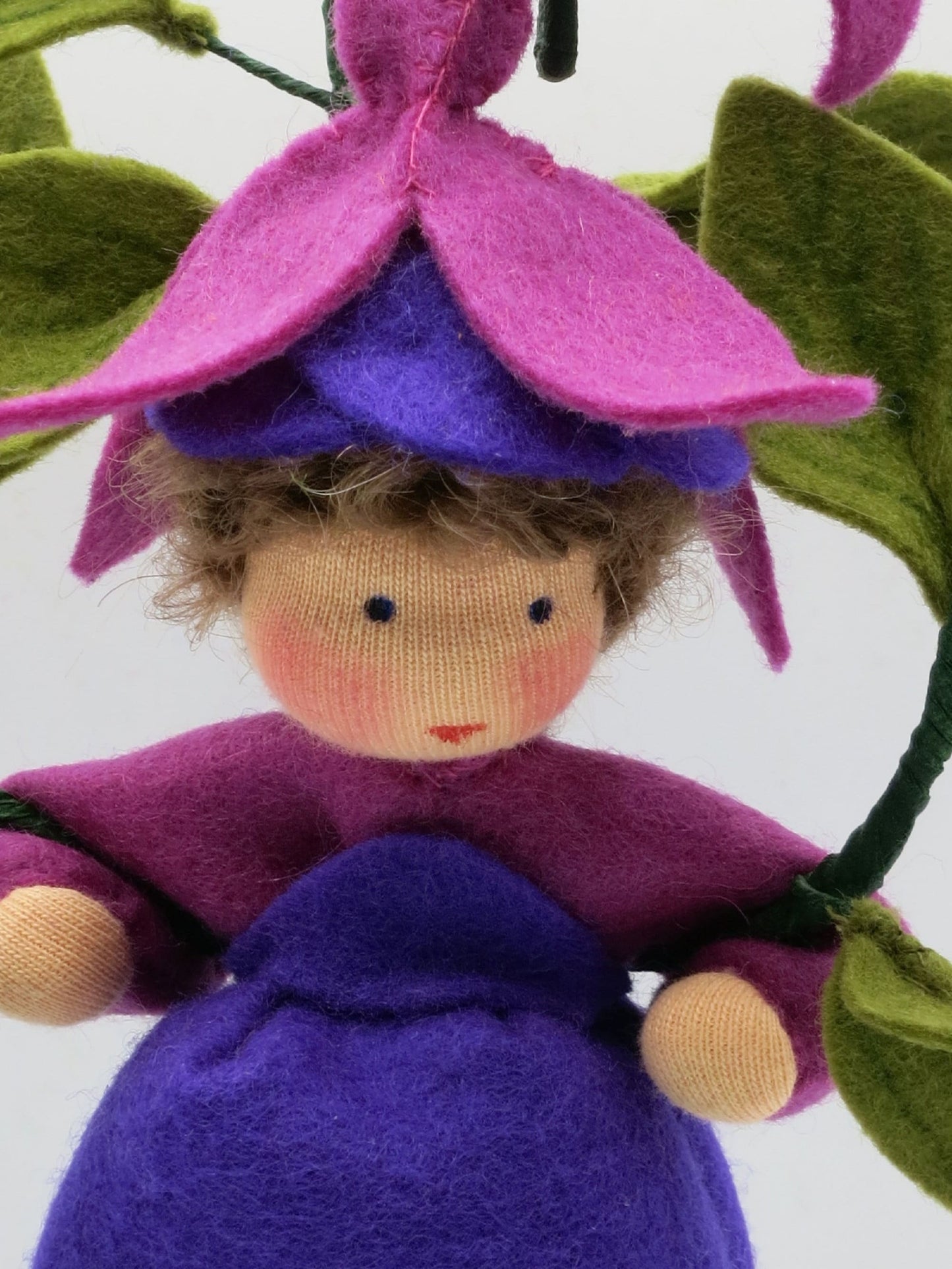 Porträt des Fuchsien-Blumenkinds aus Wollfilz mit violettem Kleid und pink-violettem Blütenhut.