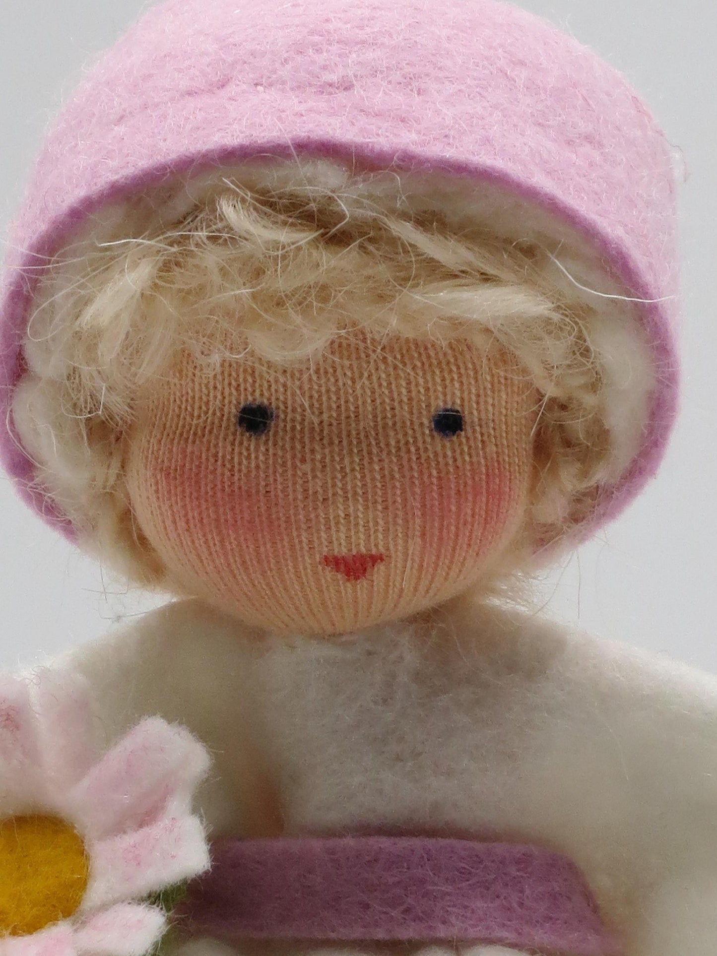 Nahaufnahme des Gesichts vom Gänseblümchen-Blumenkind mit rosa Filzhaube