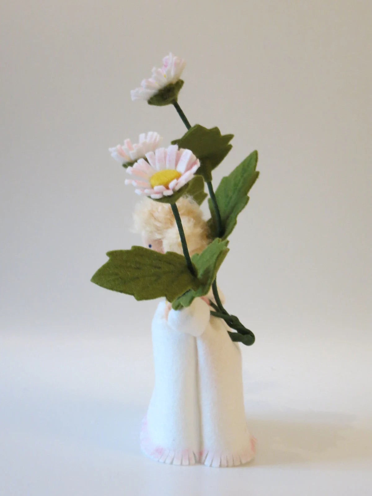 Rückansicht des Gänseblümchen-Blumenkinds mit blondem Wollhaar und grünen Blättern