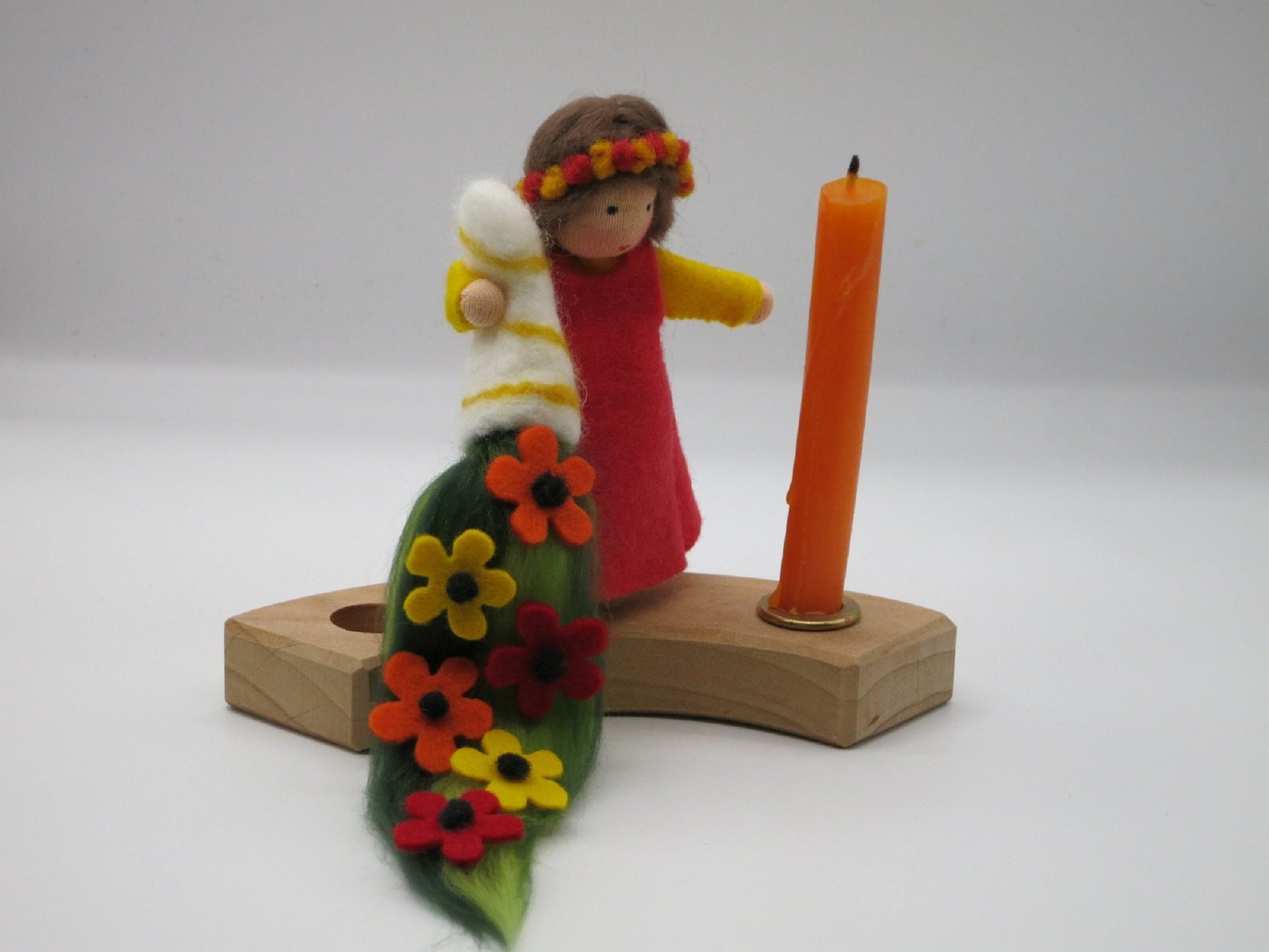 Geburtstagskind aus Wollfilz mit Blumenmantel und Geschenkkerze auf einem Holz-Kerzenring mit orangefarbener Kerze.