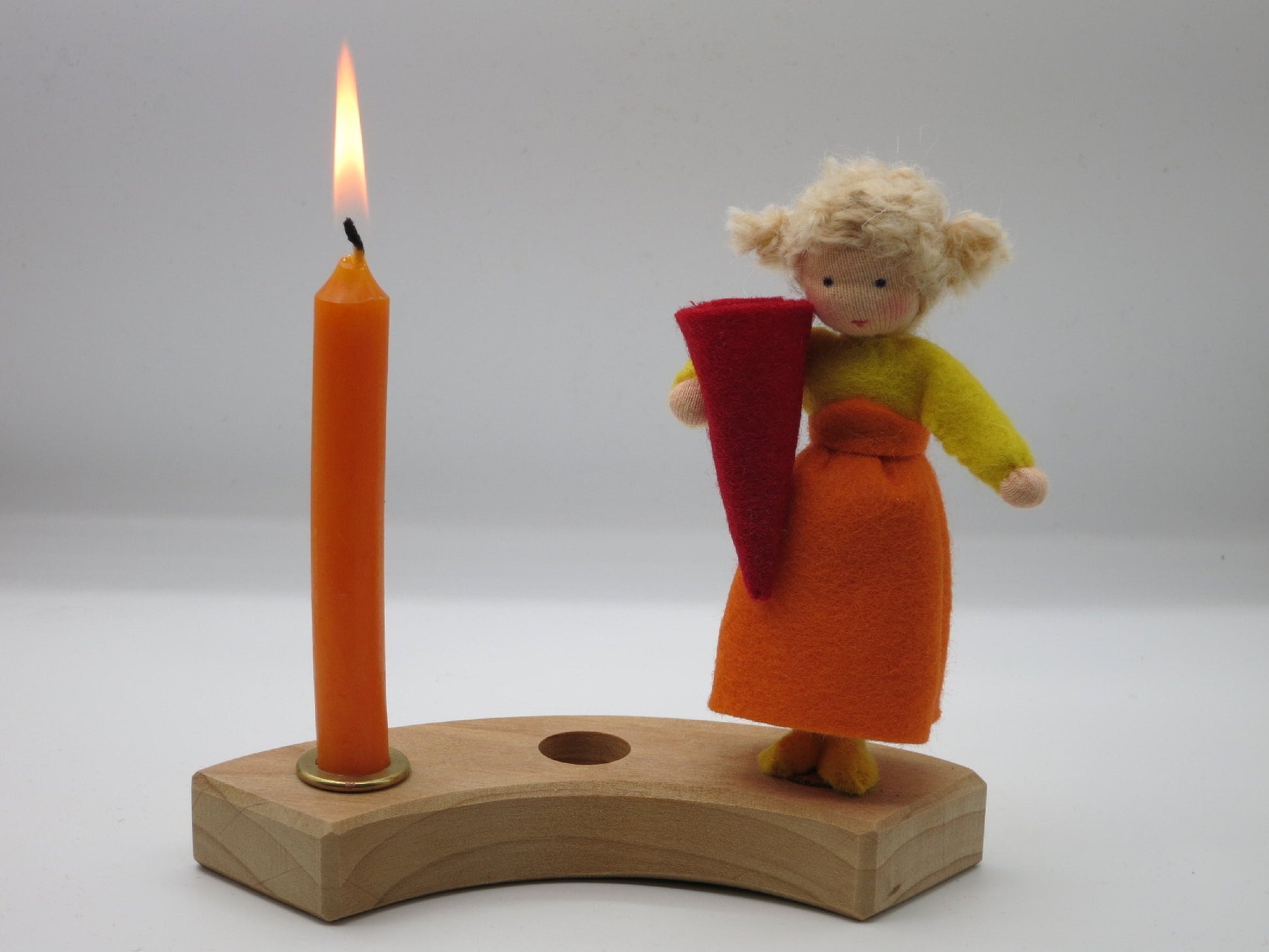 Geburtstagskind aus Wollfilz mit gelbem Oberteil, orangefarbenem Rock und roter Zuckertüte auf einem Holz-Kerzenring mit brennender Kerze.