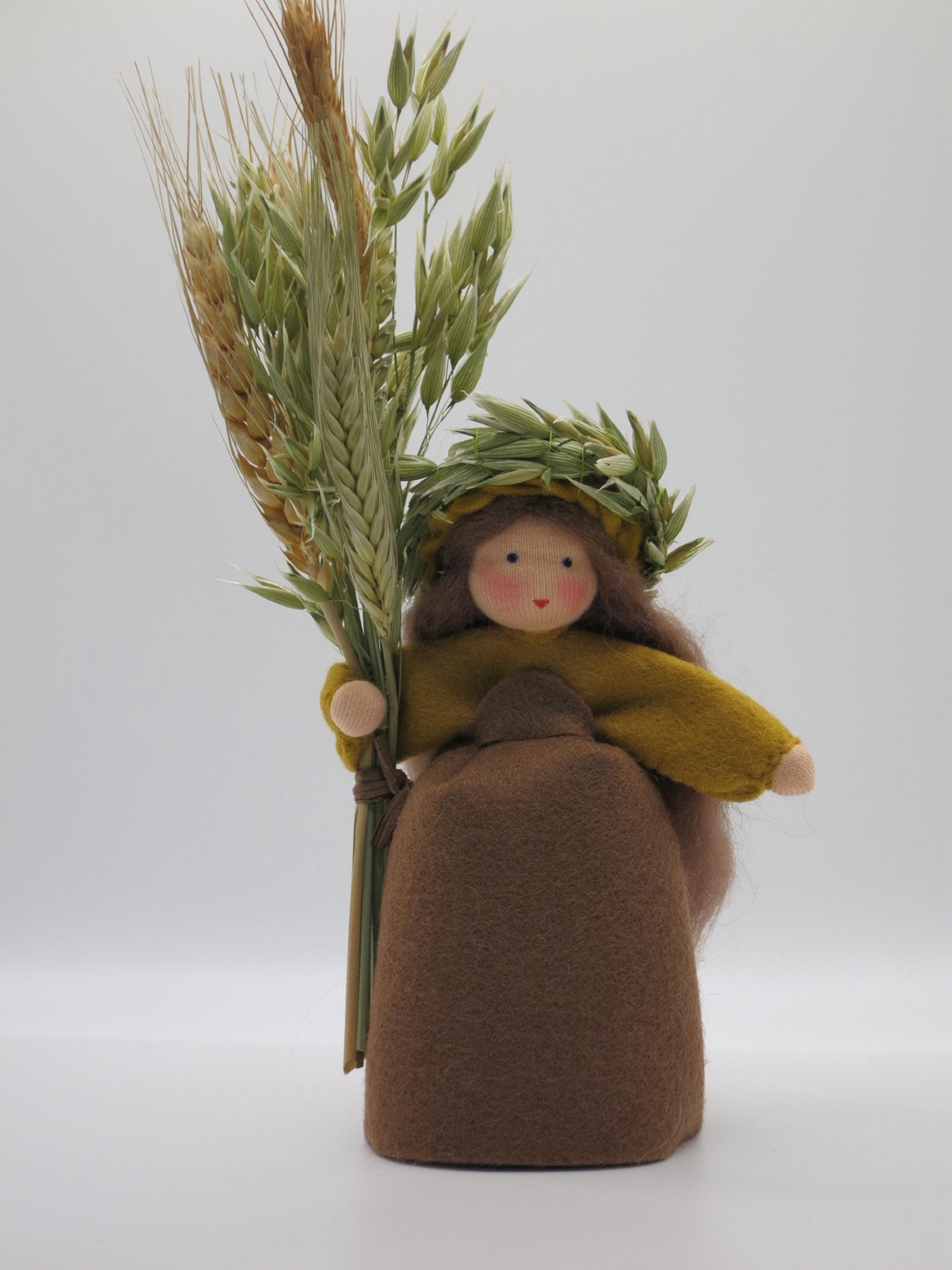 Handgefertigtes Getreidemädchen aus Wollfilz mit braunem Kleid, Ährenkranz und großer Getreidegarbe als Herbstdekoration.