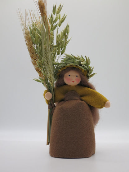 Handgefertigtes Getreidemädchen aus Wollfilz mit braunem Kleid, Ährenkranz und großer Getreidegarbe als Herbstdekoration.
