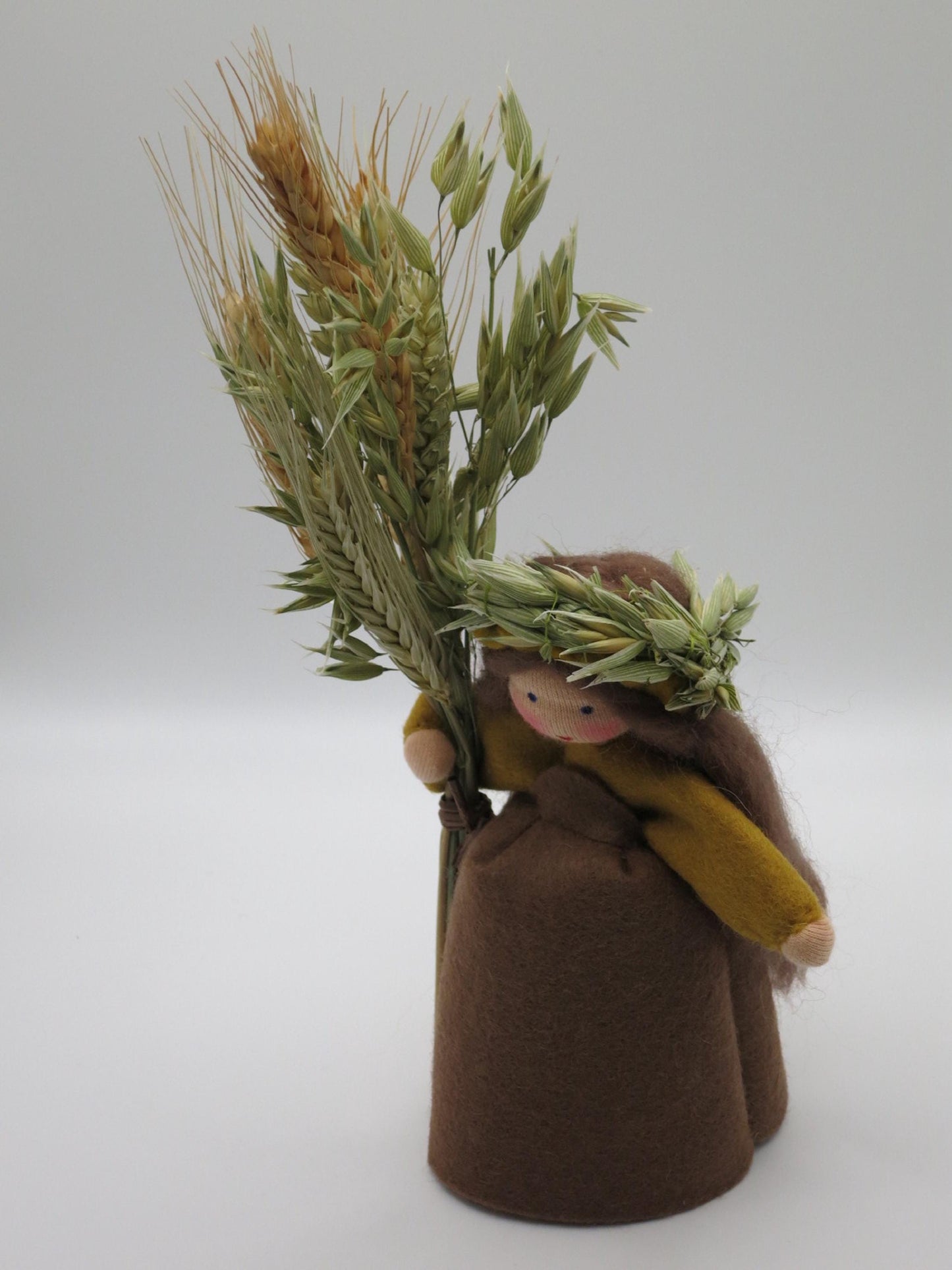 Handgefertigtes Getreidemädchen aus Wollfilz mit Ährenkranz, Getreidegarbe und gelbem Umhang als herbstliche Dekoration.