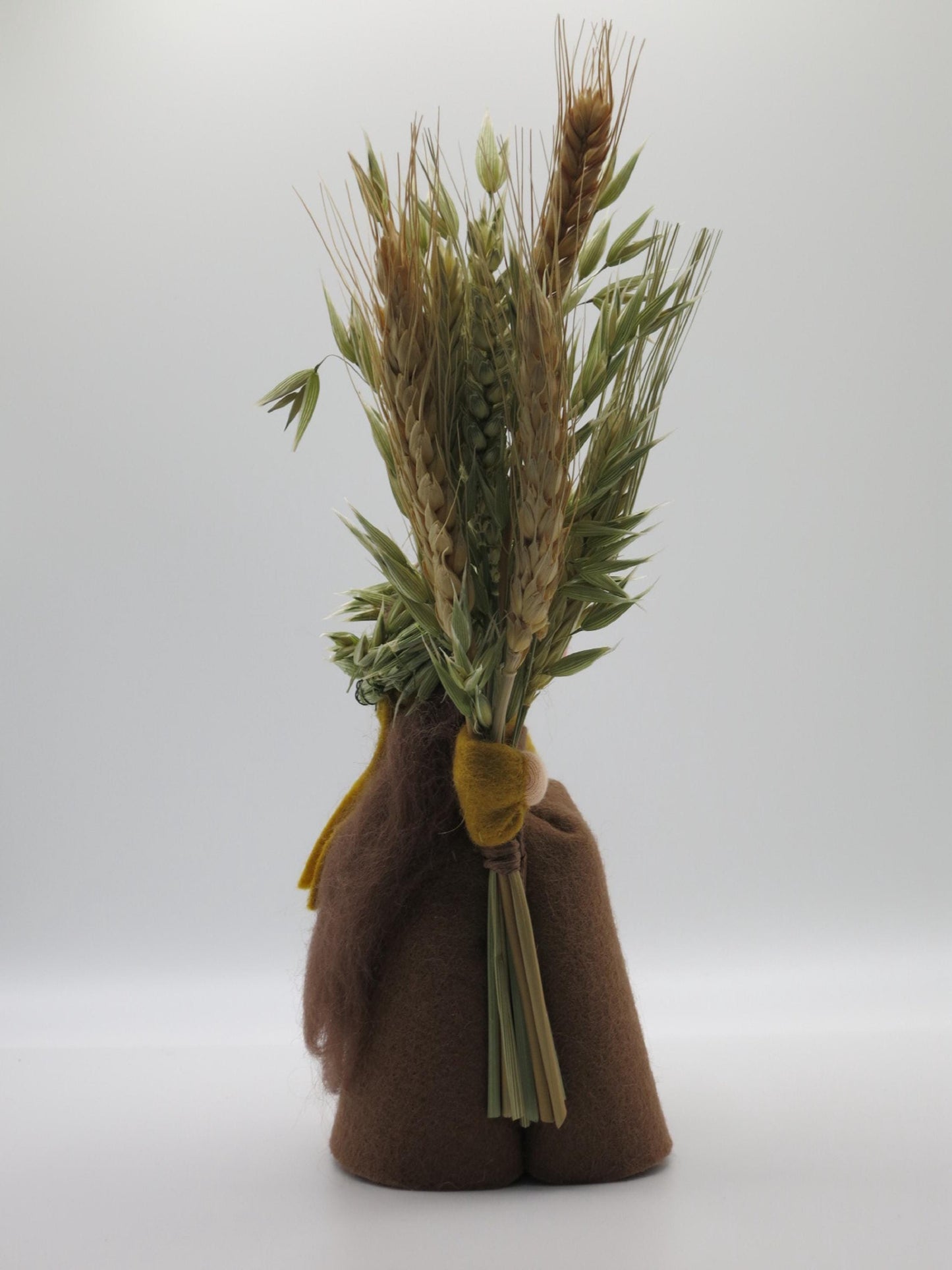 Seitenansicht des Wollfilz-Blumenkinds mit gebundener Getreidegarbe, Ährenkranz und braunem Herbstgewand.