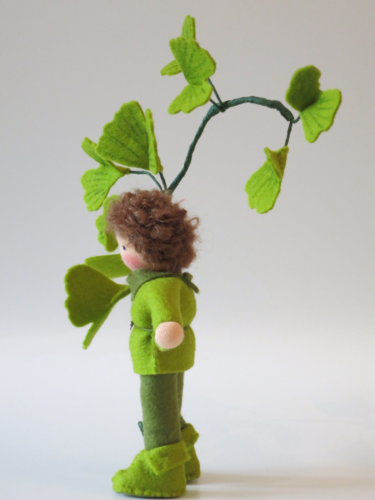 Seitenansicht des Ginkgo-Blumenkinds aus Wollfilz mit grünem Gewand, lockigem Haar und Ginkgoblättern.