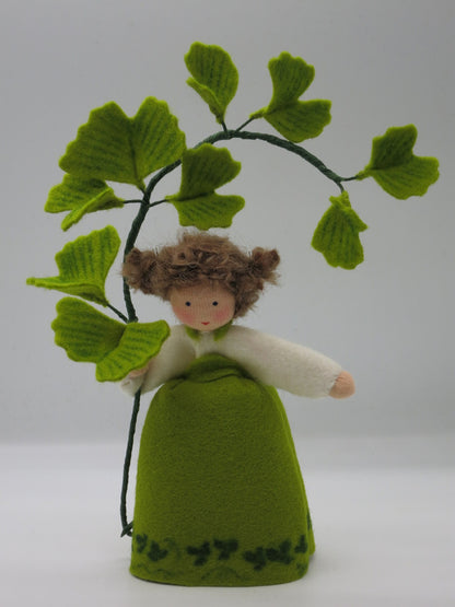 Frontalansicht des handgefertigten Ginkgo-Mädchens aus Wollfilz mit weißer Bluse, grünem Kleid und Ginkgozweig.