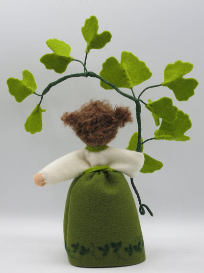 Rückansicht des Ginkgo-Mädchens aus Wollfilz mit braunem Haar, grünem Kleid und Zweig mit Ginkgoblättern.
