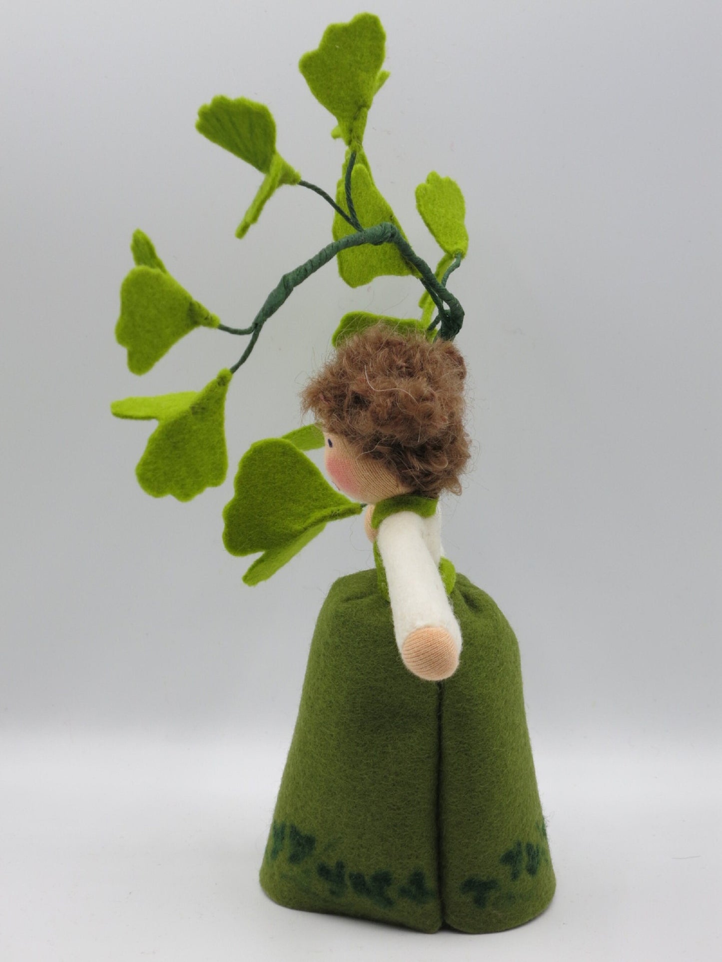 Seitenansicht des Ginkgo-Mädchens aus Wollfilz mit grünem Kleid, braunem Haar und Ginkgozweig.