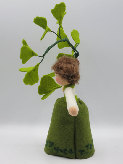 Seitenansicht des Ginkgo-Mädchens aus Wollfilz mit grünem Kleid, braunem Haar und Ginkgozweig.