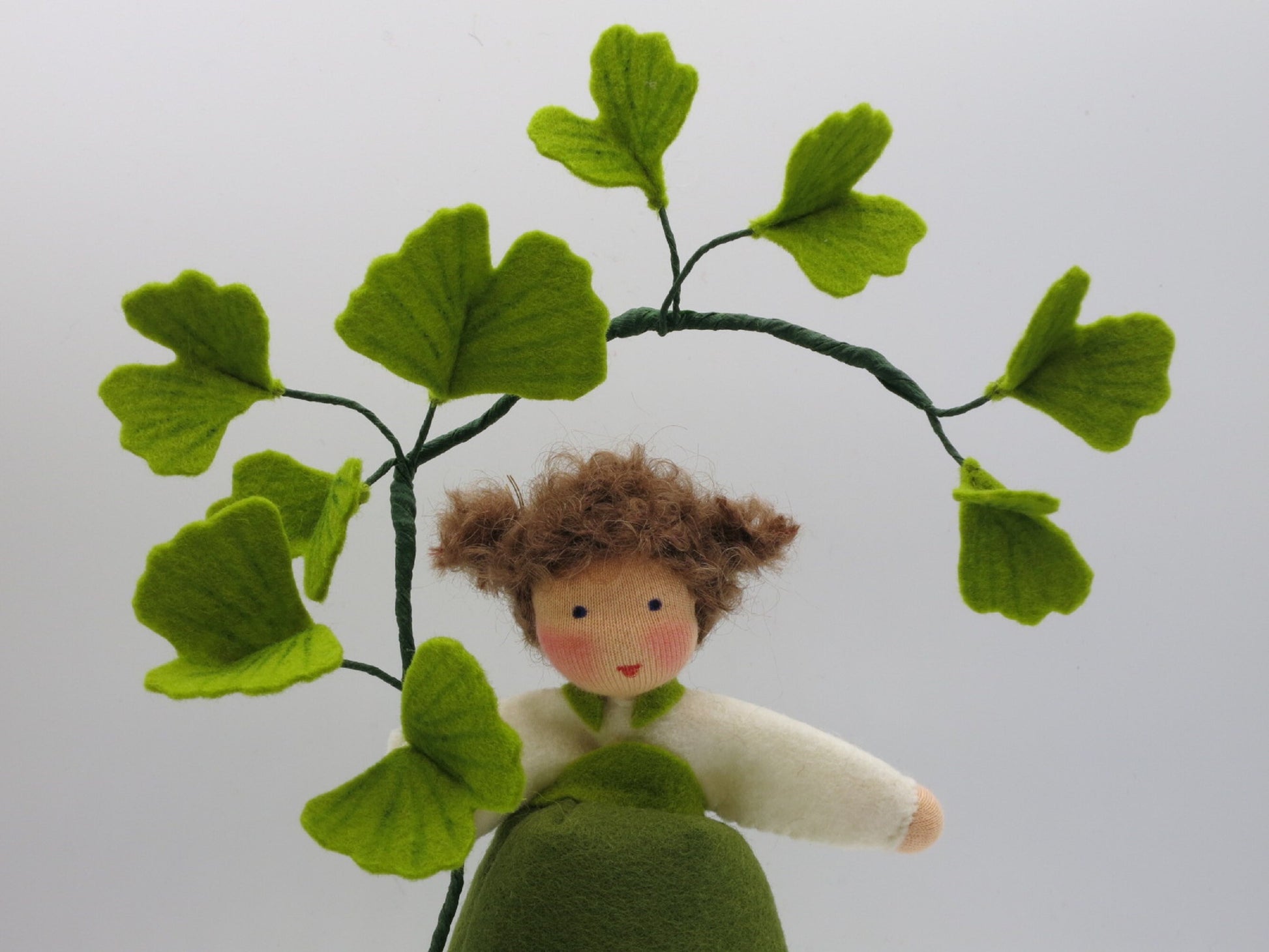 Detailansicht des Ginkgo-Mädchens aus Wollfilz mit braunem Haar und einem Zweig aus fächerförmigen Ginkgoblättern.