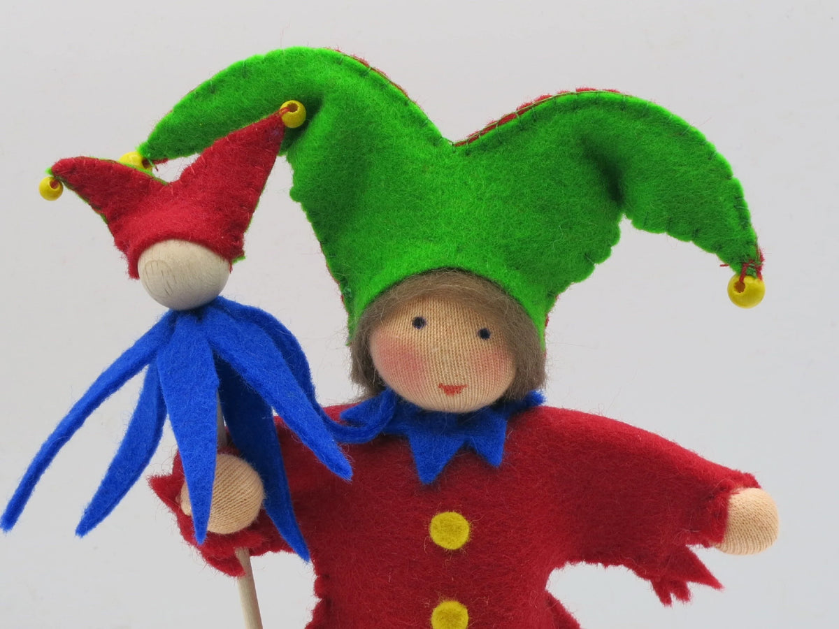 Porträt des Harlekin-Blumenkinds mit grün-roter Zipfelmütze, Glöckchen und Marotte in der Hand