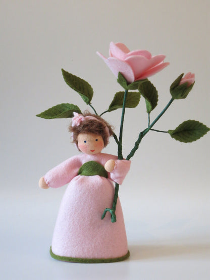 Heckenröschen-Blumenkind aus Wollfilz mit braunem Lockenhaar und rosa Blüte am Zweig, Waldorf-Figur für den Sommer-Jahreszeitentisch.
