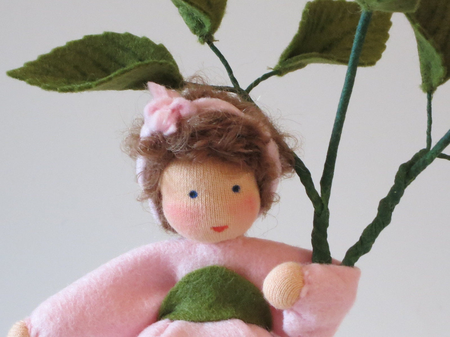 Gesichtsdetail des Heckenröschen-Blumenkinds mit braunem Lockenhaar und rosa Schleife.