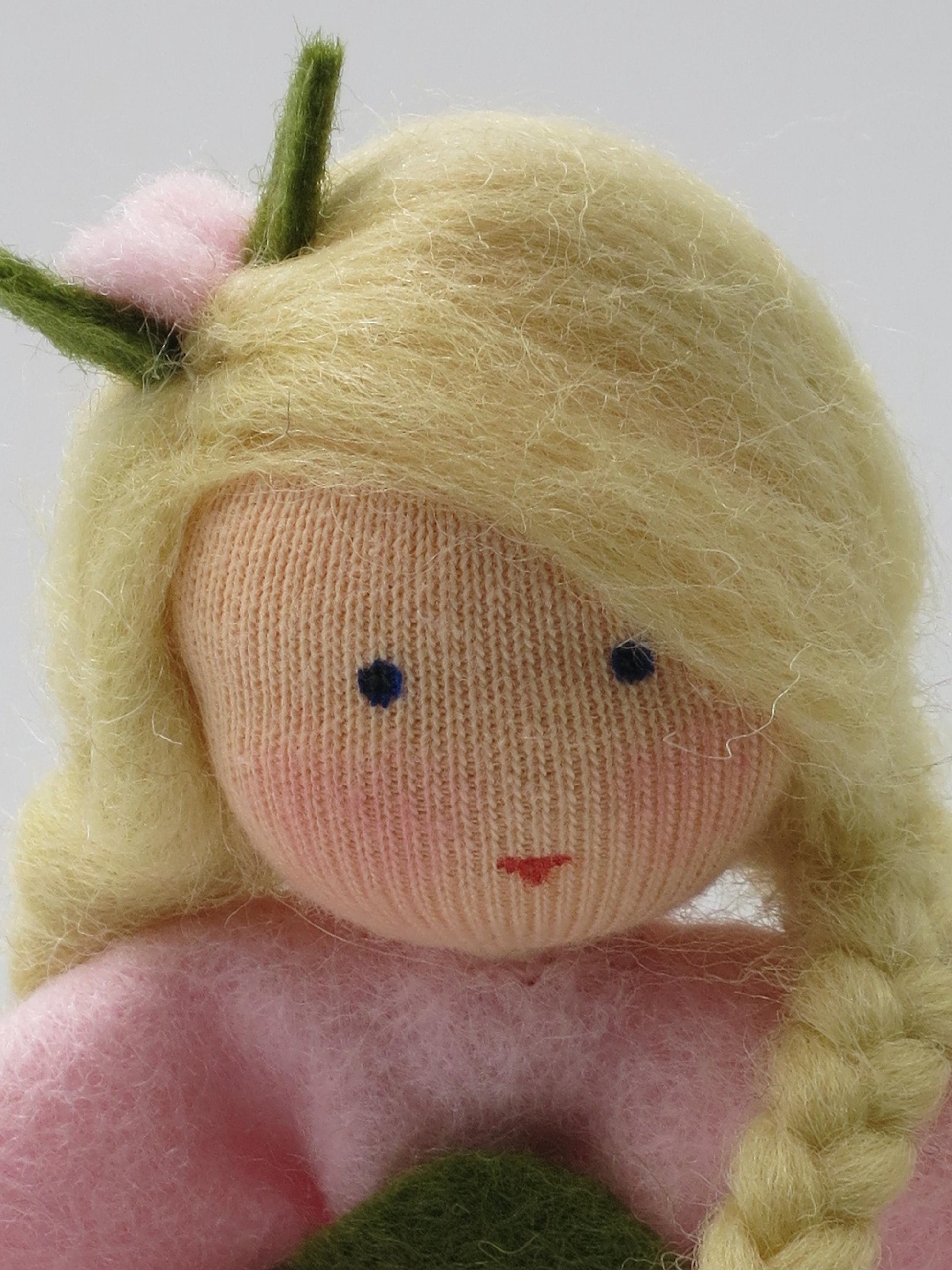 Gesichtsdetail des Heckenröschen-Blumenkinds mit blondem Haar, geflochtenem Zopf und rosa Blütenschmuck im Haar.