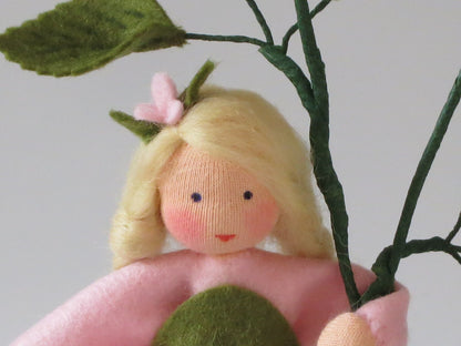 Nahaufnahme von Gesicht und Blütenzweig des Waldorf-Heckenröschens mit gestickten Augen und rosa Wangen.