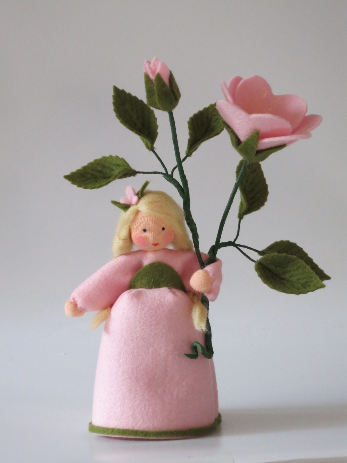 Heckenröschen-Blumenkind aus Wollfilz mit rosa Heckenrosen-Blüte und Knospe am Zweig, Waldorf-Figur für den Sommer-Jahreszeitentisch.