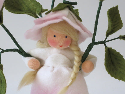 Porträt des Heckenrose-Blumenkindes mit rosa Blütenhütchen und blondem Zopf, Waldorf Jahreszeitentisch.