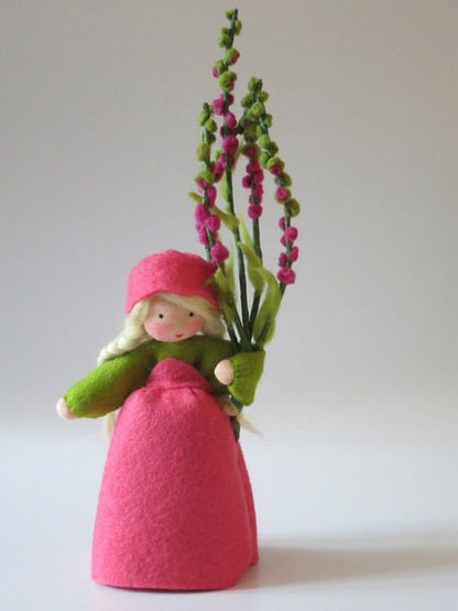 Heidekraut-Erika-Blumenkind aus Wollfilz für den Waldorf Jahreszeitentisch, hält einen Strauß aus vier Blütenrispen in Gelbgrün und Magenta.