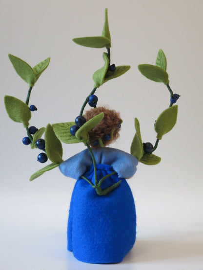Rückansicht des Heidelbeere-Blumenkindes mit Beerenkranz im Lockenhaar und blauem Wollfilzkleid.