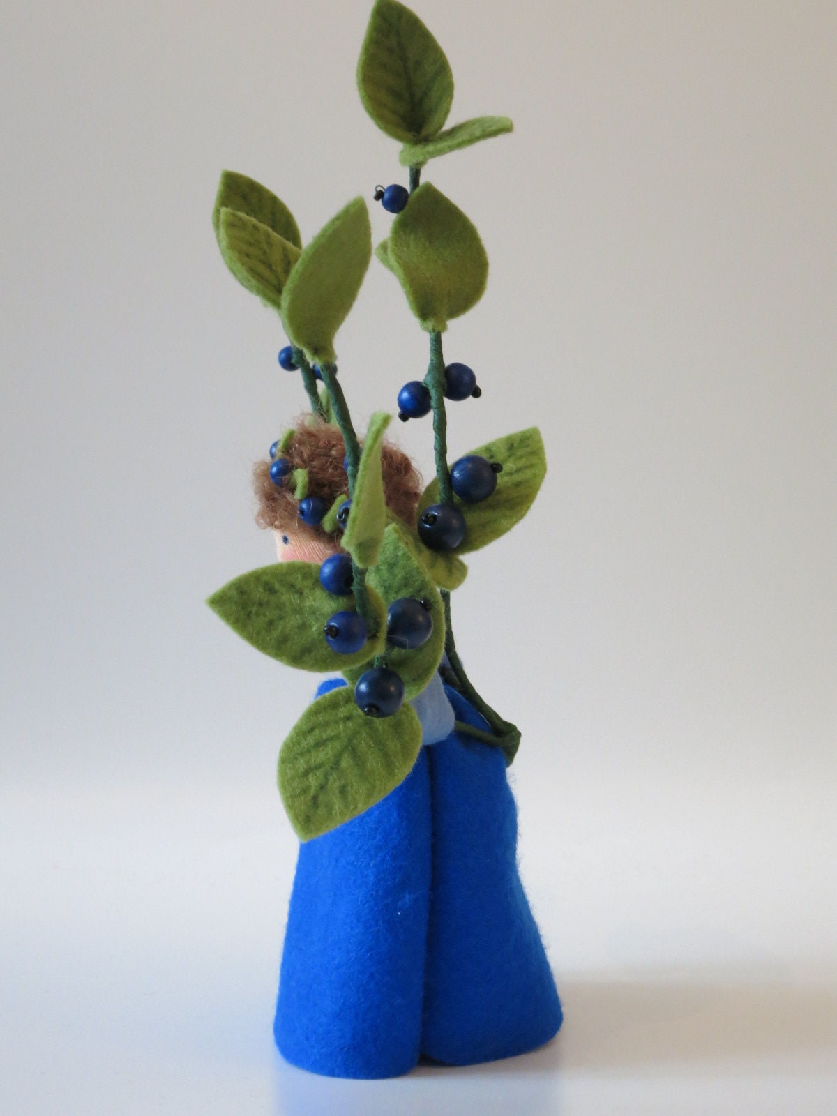 Nahaufnahme des Gesichts der Heidelbeere-Figur mit Beerenkranz im Haar, Wollfilz-Blumenkind für den Jahreszeitentisch.