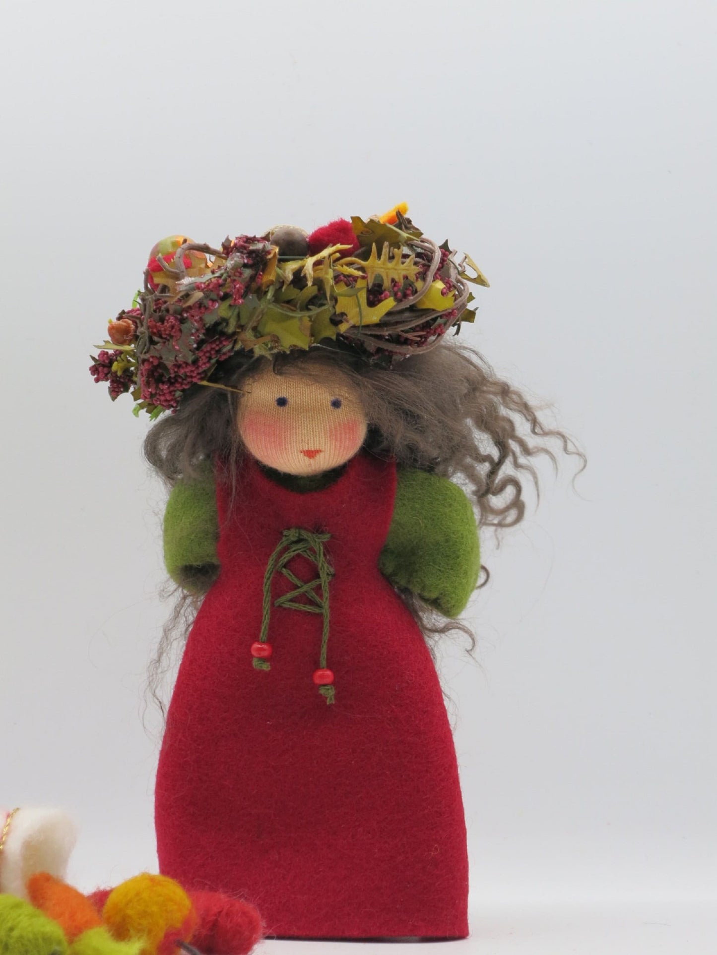 Handgefertigte Herbstfigur im roten Filzkleid mit grauem Wollhaar und üppigem Kranz aus Blättern, Beeren und Naturmaterialien