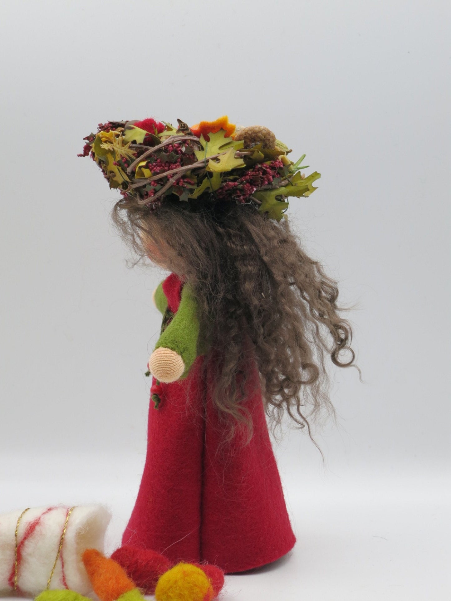 Seitliche Ansicht der Herbstfigur mit langem grauem Lockenhaar, rotem Filzkleid und herbstlichem Naturkranz