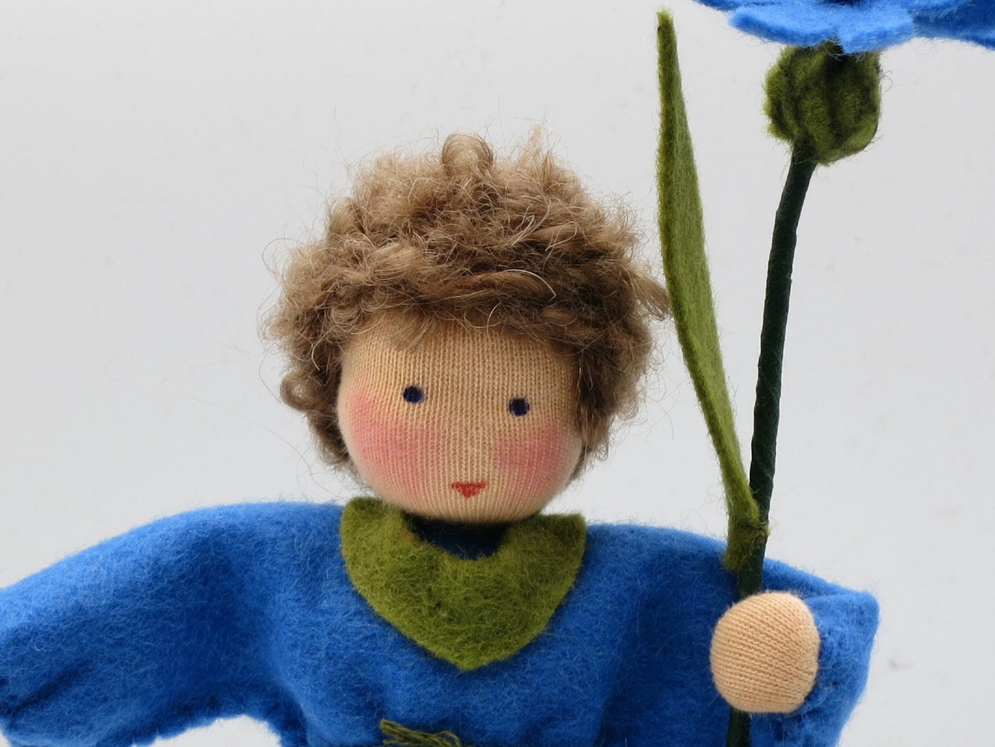 Gesichtsdetail des Kornblume-Blumenkinds mit lockigem braunem Haar und grünem Halstuch aus Wollfilz.