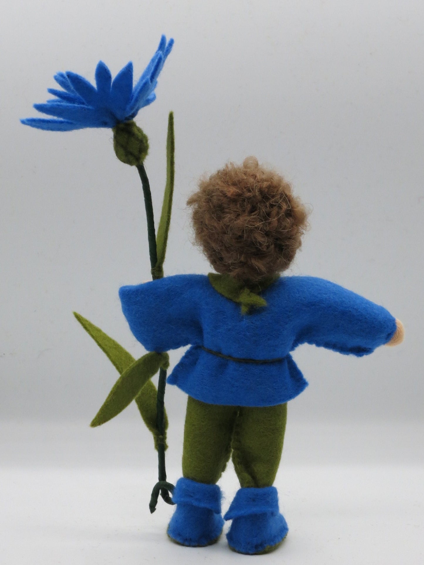 Rückansicht des Kornblume-Blumenkinds mit lockigem Haar und blauen Filzstiefeln, Wollfilz-Handarbeit.
