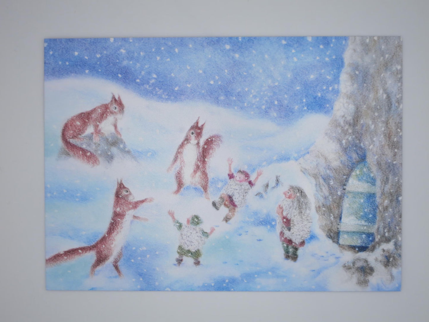 Kunst-Postkarte „Winterfreuden“ von Monika Speck: Eichhörnchen spielen mit Wichtelkindern im Schnee, Postkarte für Kinder in Buntstift-Technik