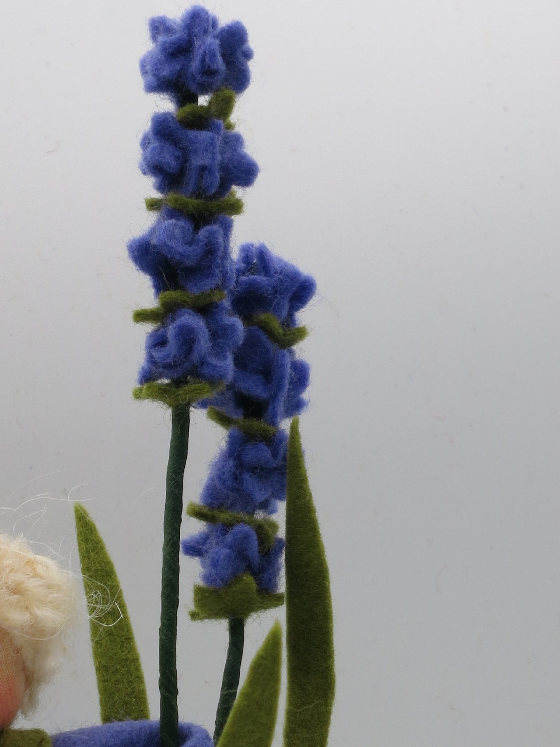 Nahaufnahme der lila Filzblütenrispen am Lavendel-Junge, Waldorf-Wollfilzfigur