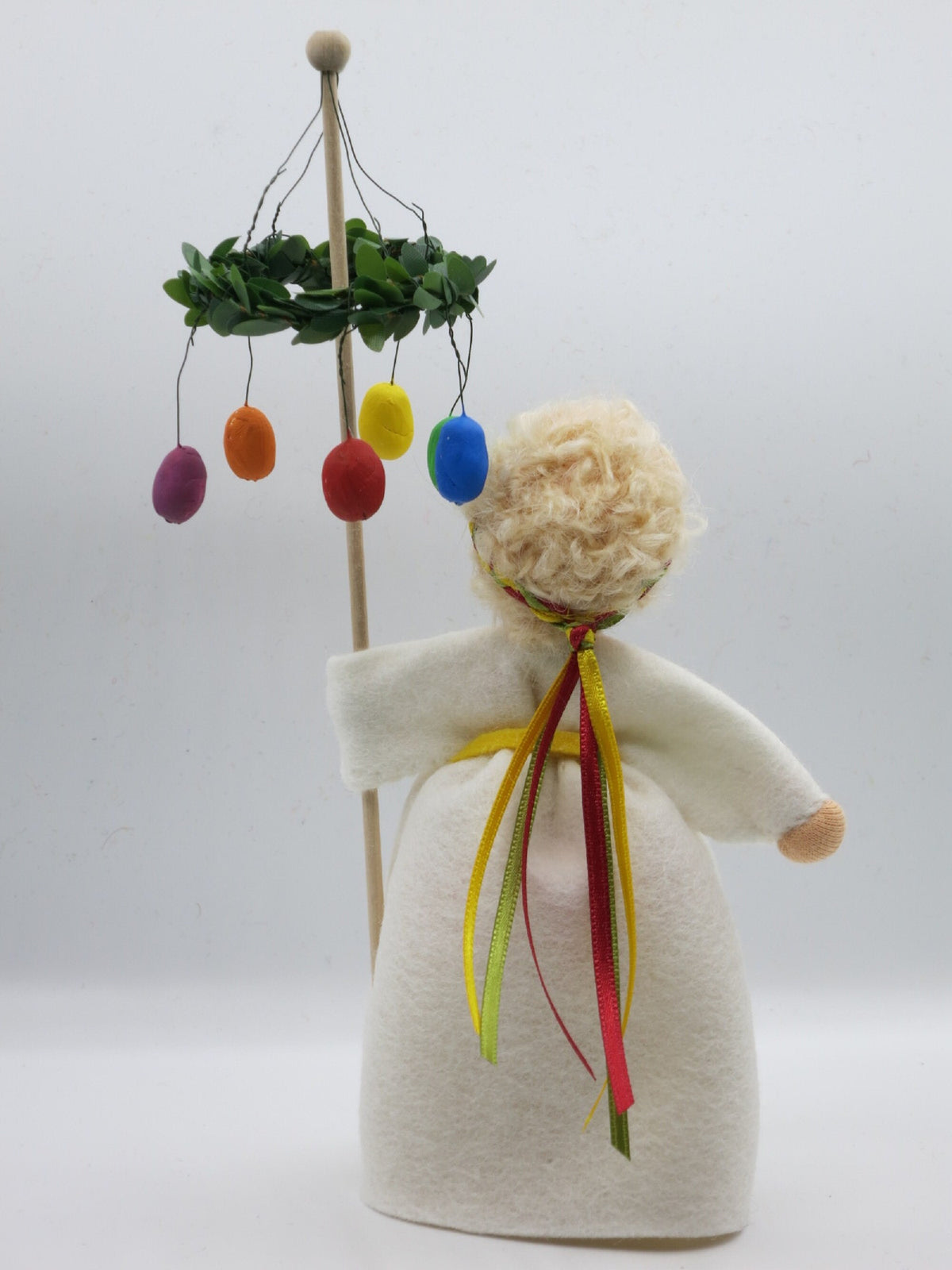 Osterkranz-Blumenkind schräg von hinten mit bunten Bandschleifen am Rücken und Blick auf den Eierkranz