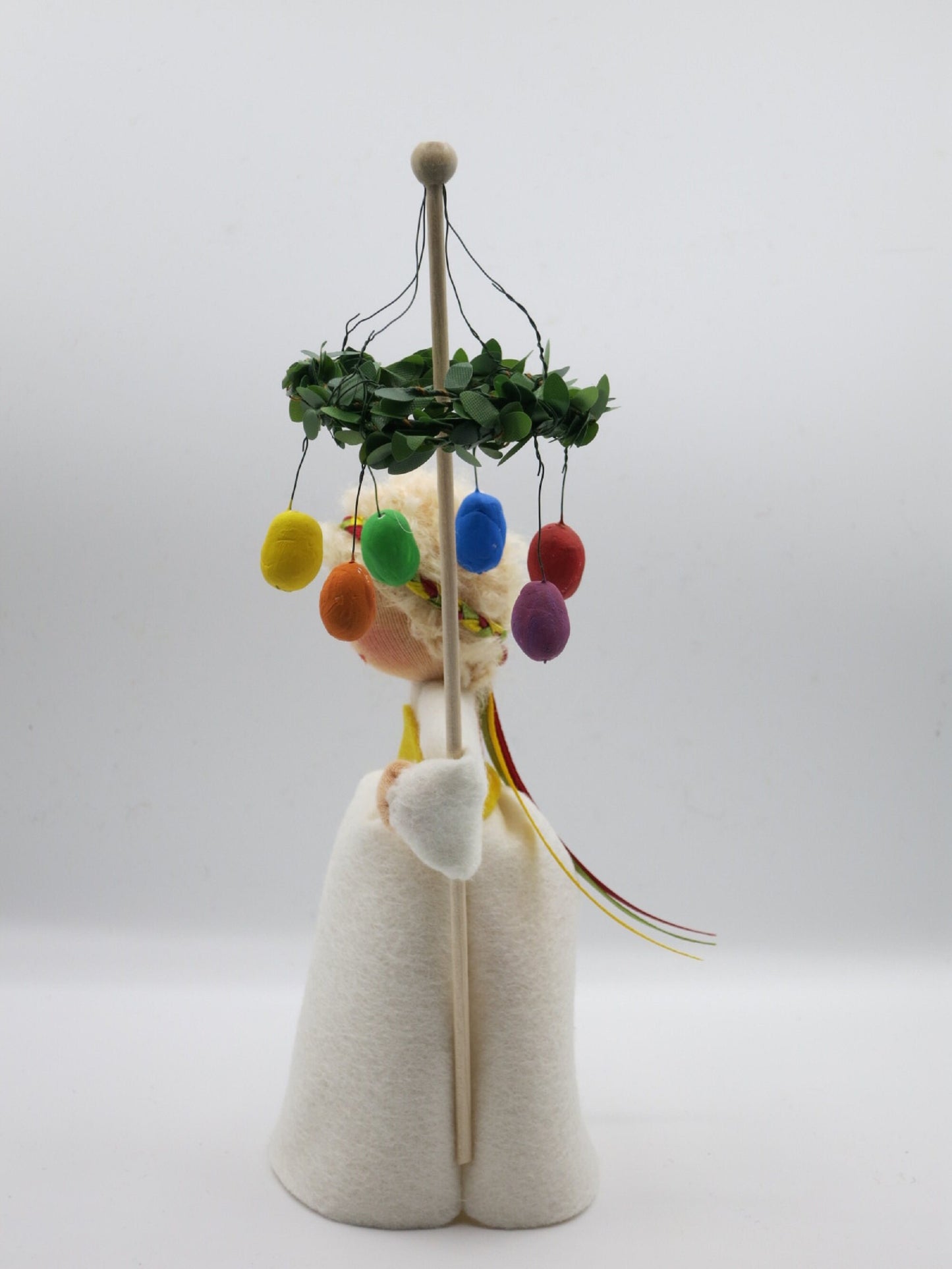 Rückansicht des Osterkranz-Blumenkinds mit Buchsbaumkranz und bunten Ostereiern am Stab