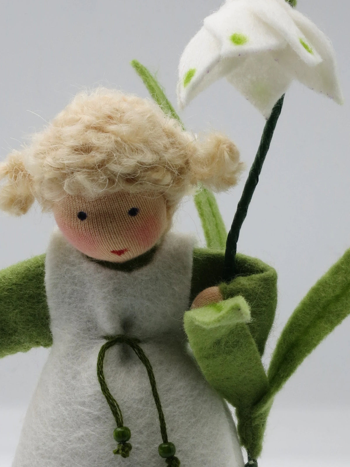 Porträt des Märzenbecher-Blumenkinds mit blondem Lockenhaar, Zöpfchen und weißer Filzblüte im Hintergrund
