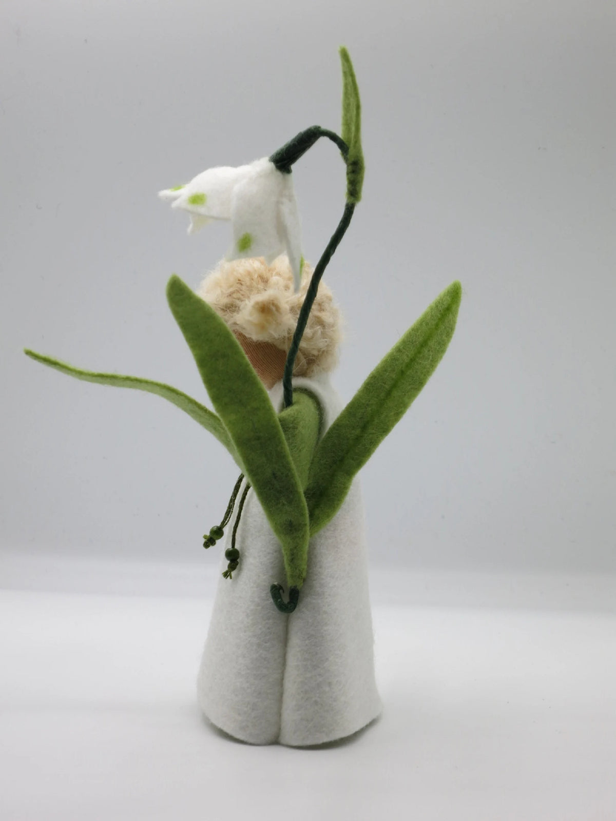Märzenbecher-Blumenkind von hinten mit geschwungenem Blütenstiel und grünen Blättern