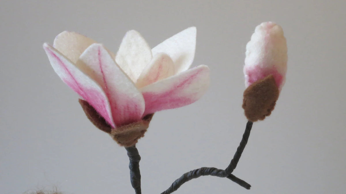 Detailansicht der weiß-rosa Magnolienblüte aus Filz mit brauner Knospe am Zweig