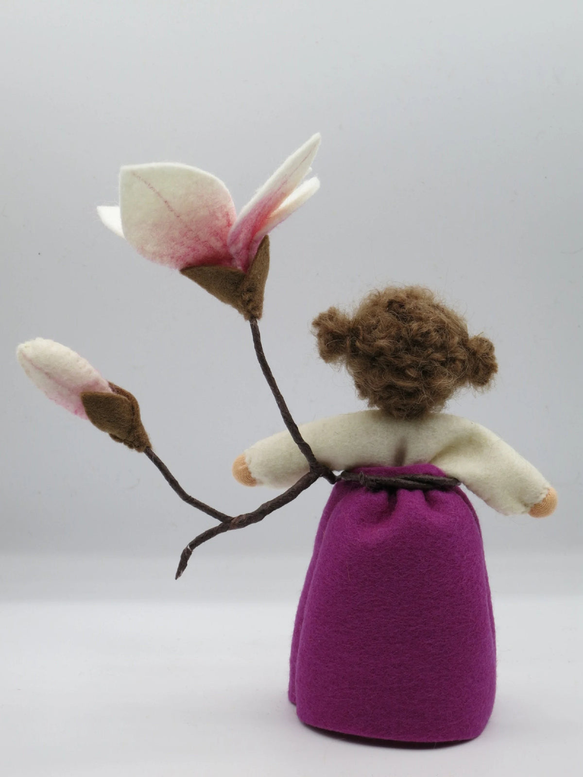 Rückansicht des Magnolie-Blumenkinds mit braunem Lockenhaar und Magnolienzweig für den Waldorf Jahreszeitentisch
