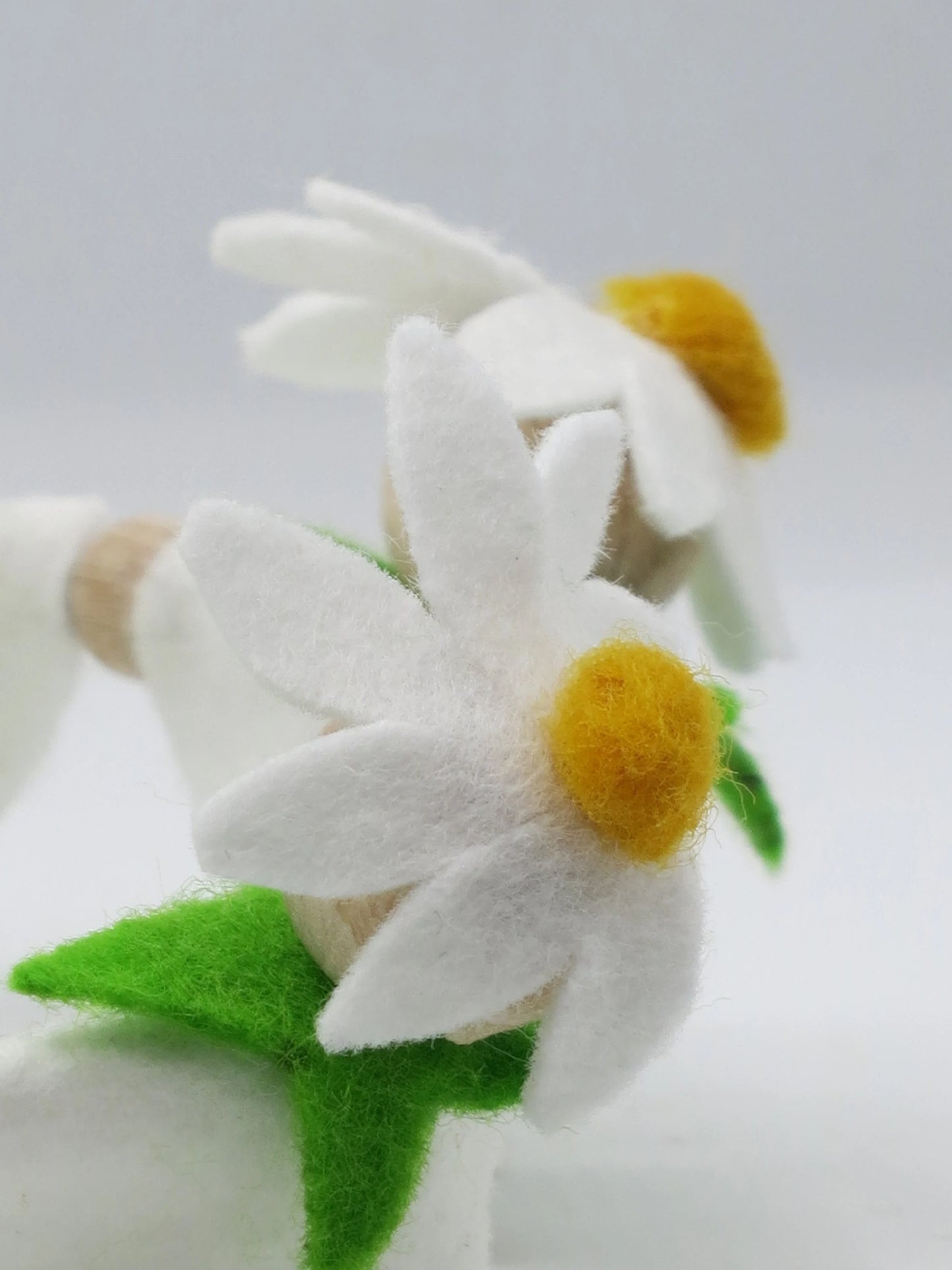 Nahaufnahme einer weißen Margeritenblüte aus Filz mit gelber Blütenmitte und grünen Blättern am Blumenkind.