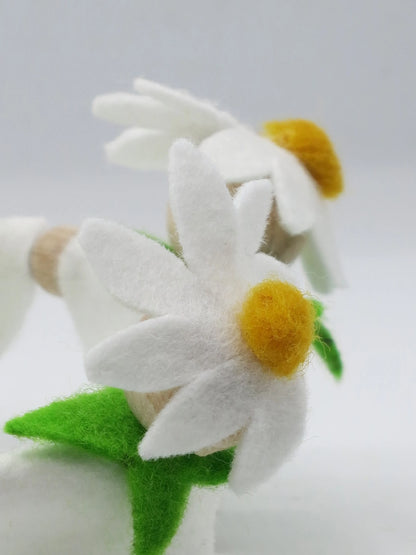 Nahaufnahme einer weißen Margeritenblüte aus Filz mit gelber Blütenmitte und grünen Blättern am Blumenkind.