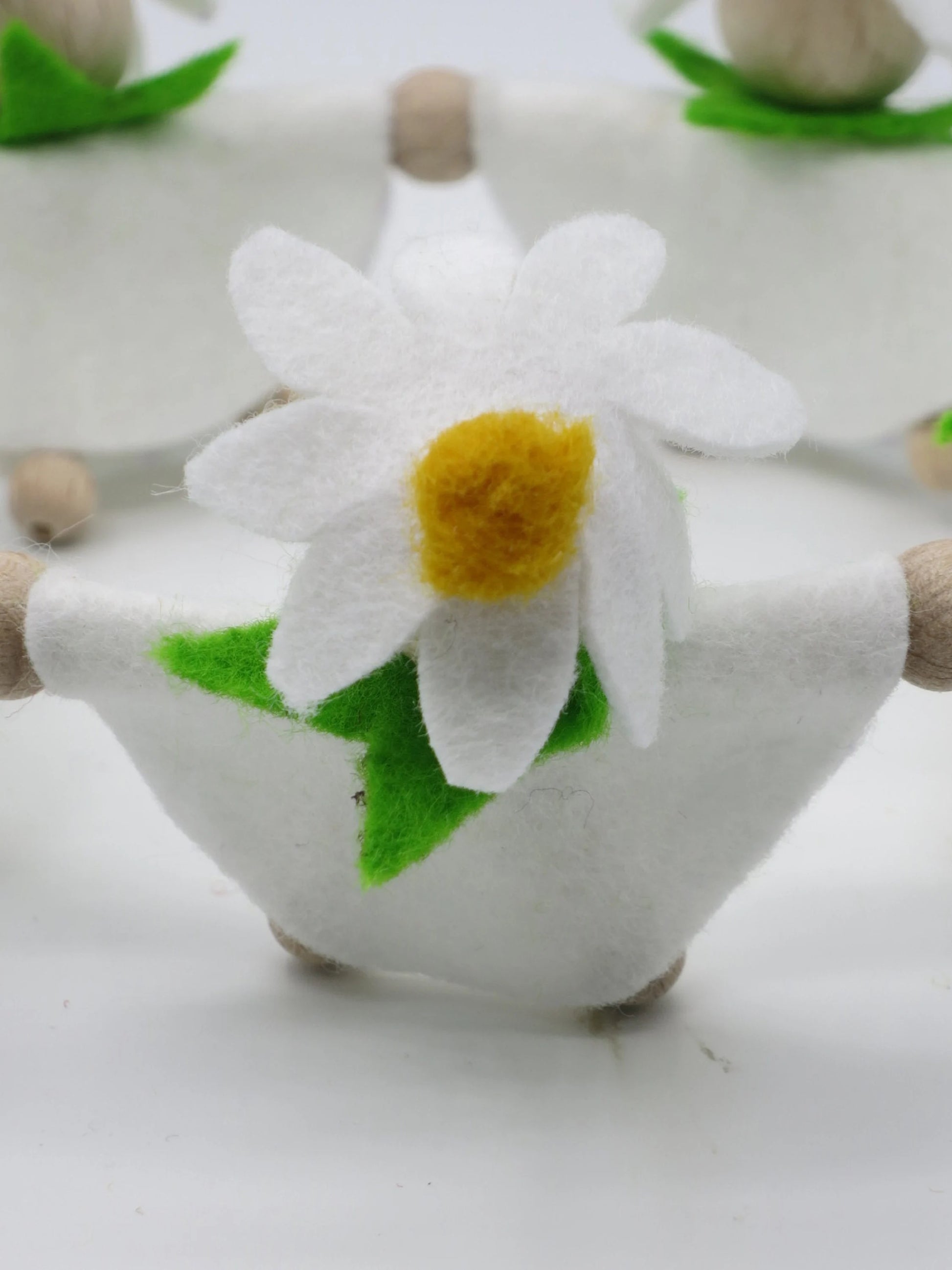 Vorderansicht eines handgefertigten Margeriten-Blumenkinds mit weißem Filzkleid, grünen Blättern und großer Blüte.