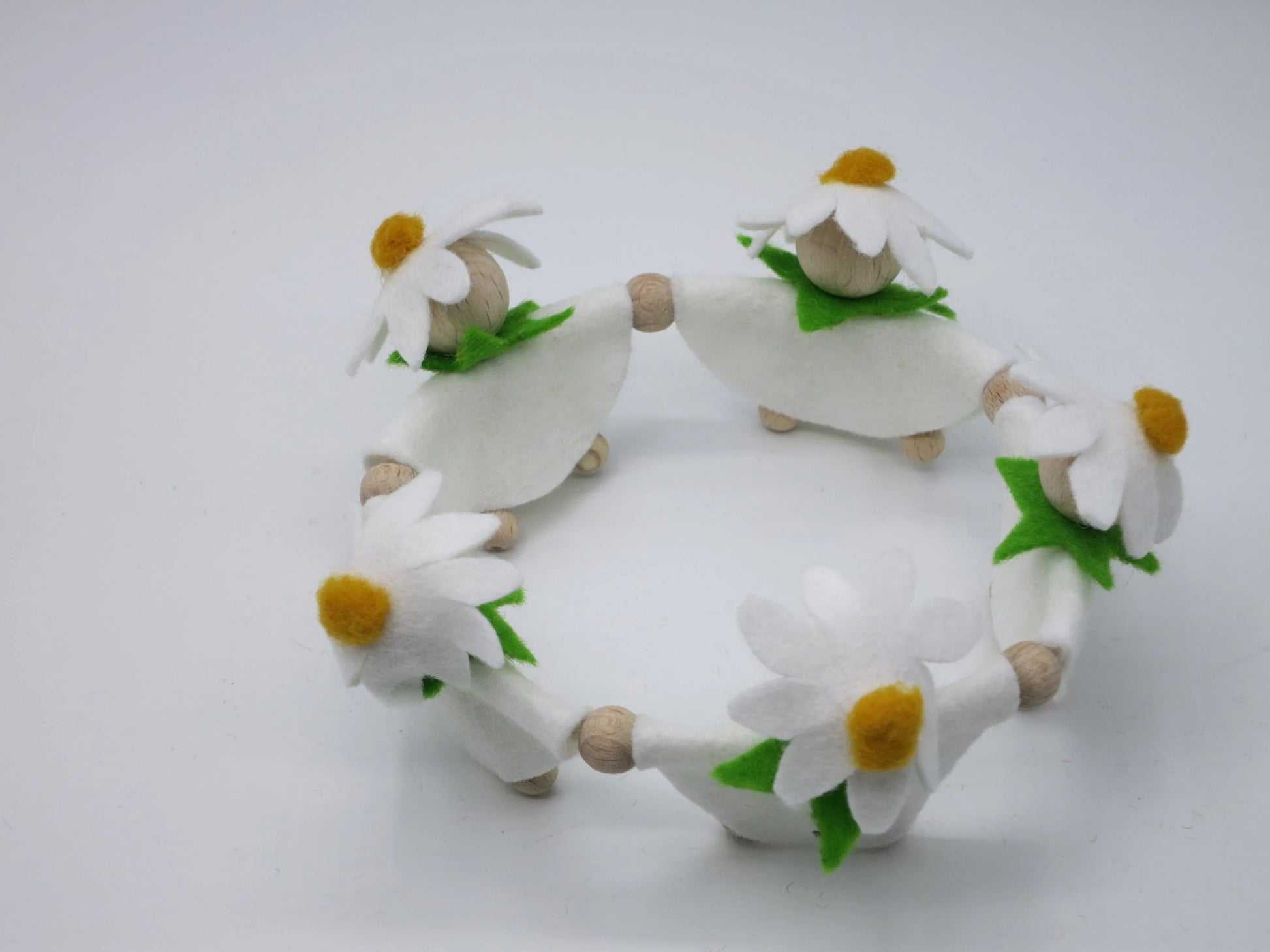 Draufsicht auf fünf Margeriten-Blumenkinder in weißen Filzkleidern, die gemeinsam einen runden Frühlingskranz bilden.