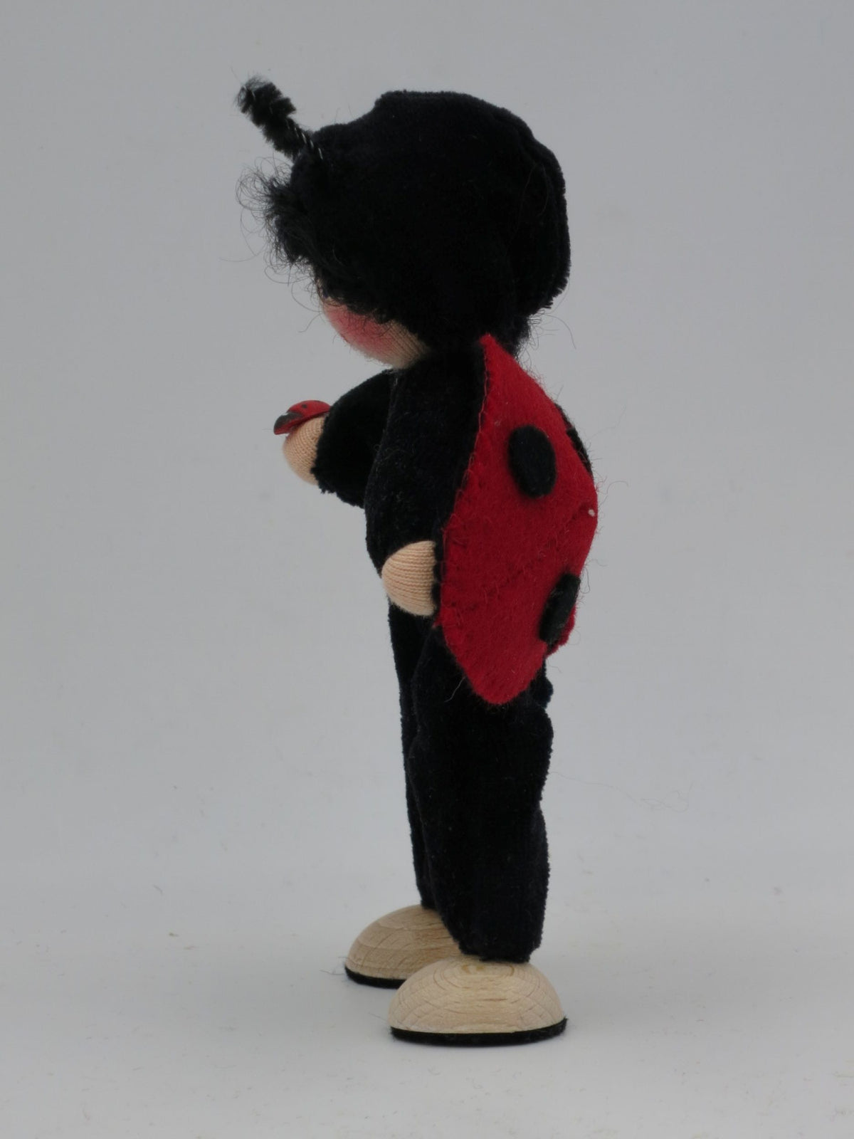Marienkäfer-Blumenkind im Profil mit rotem Punktflügel und kleiner Marienkäfer-Holzfigur in der Hand