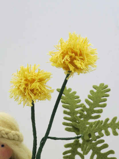 Zwei gelbe Mimosenblüten aus Wollgarn mit grünem Filzfarn am Blumenkind