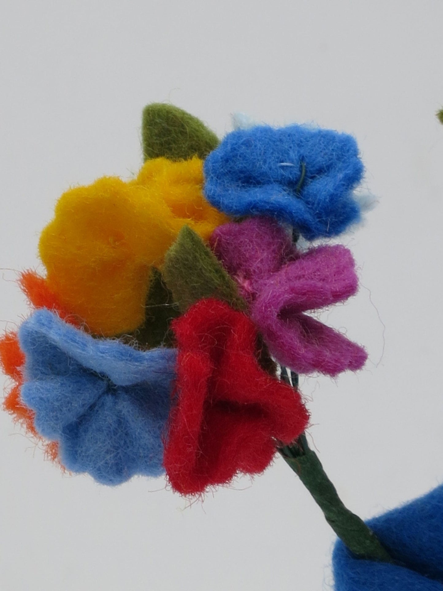 Detailaufnahme des bunten Filz-Blütenstraußes des Mittsommer-Jungen in Gelb, Blau, Orange und Rot.